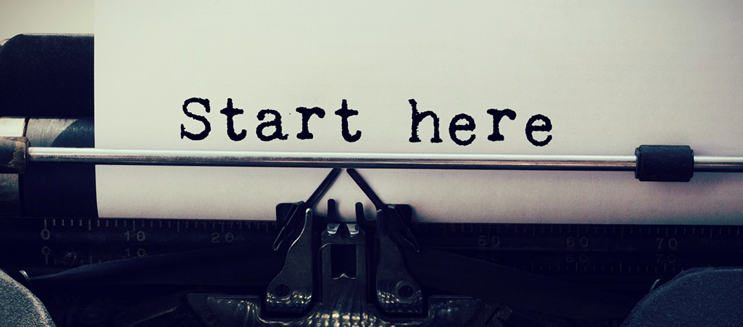 Typewriter loaded with paper and the words "start here" printed on the paper