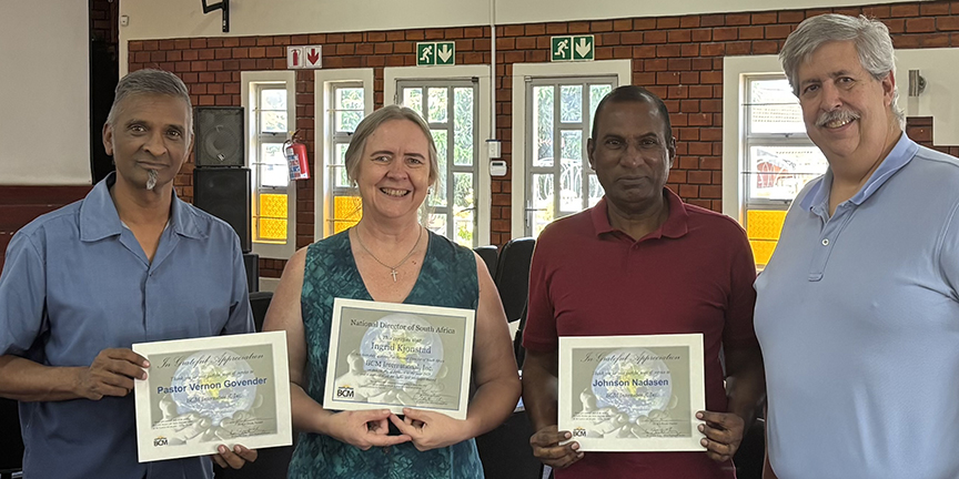 Three people in a row holding certificates of achievement with one other person presenting certificates.