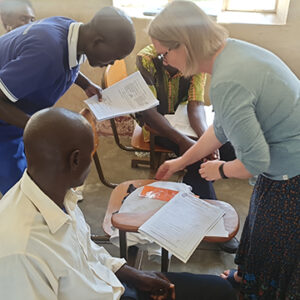 Ingrid points to papers on a desk in a classroom with other students