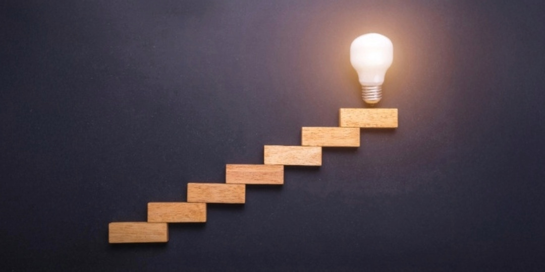 wooden blocks placed as stairs leading up to a lit lightbulb